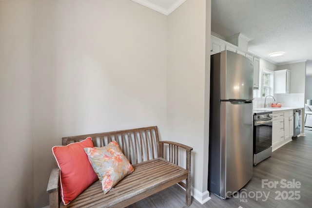 kitchen featuring a sink, stainless steel appliances, crown molding, white cabinets, and wood finished floors