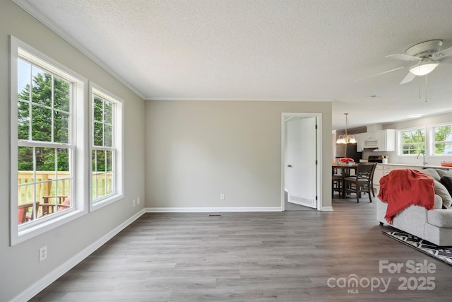 living room with baseboards, wood finished floors, ceiling fan with notable chandelier, and a textured ceiling