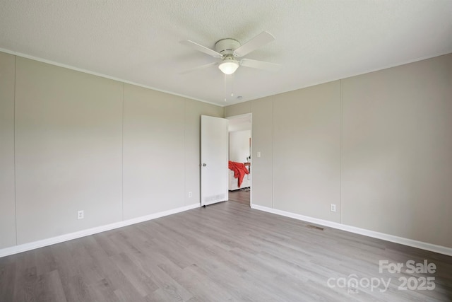 empty room with wood finished floors, ceiling fan, baseboards, visible vents, and a textured ceiling