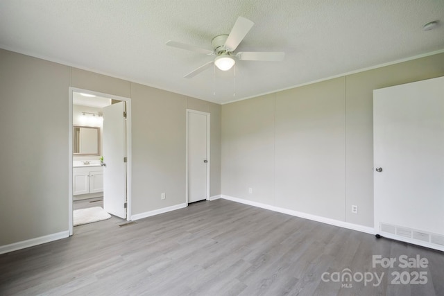 unfurnished bedroom with a textured ceiling, wood finished floors, ensuite bathroom, and visible vents