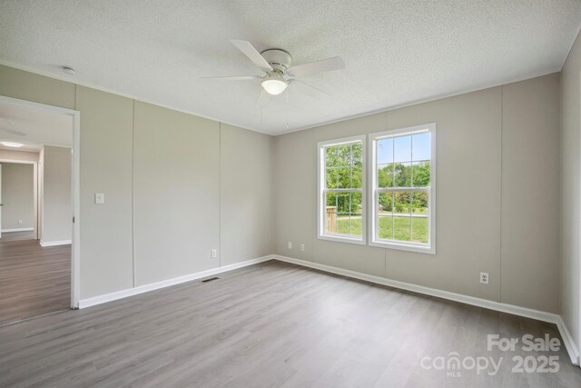 spare room featuring a textured ceiling, wood finished floors, a ceiling fan, and visible vents