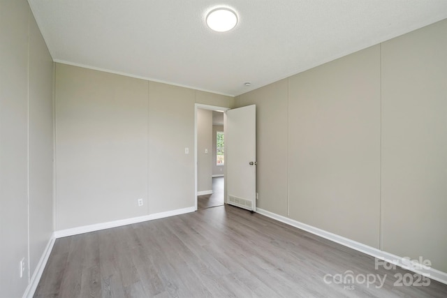 spare room featuring baseboards, wood finished floors, and crown molding