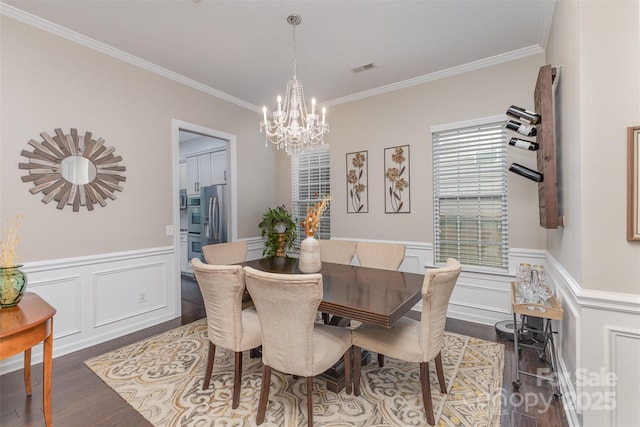 dining area with a wainscoted wall, wood finished floors, a chandelier, and crown molding