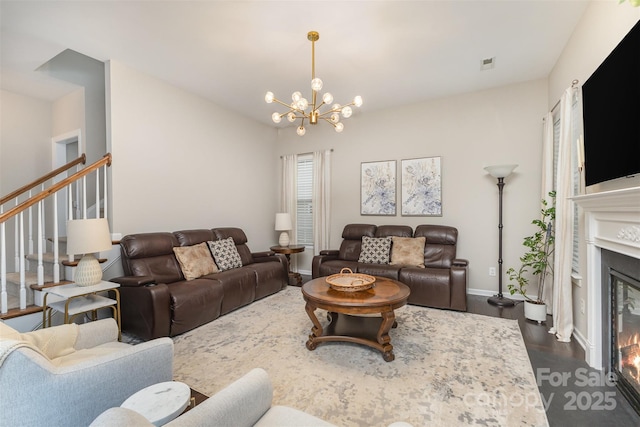 living area featuring a notable chandelier, stairs, a glass covered fireplace, baseboards, and dark wood-style flooring