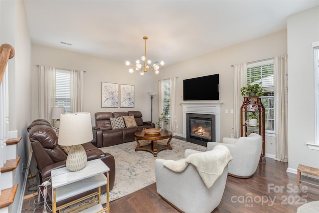 living area with a fireplace with flush hearth, dark wood finished floors, a notable chandelier, and visible vents