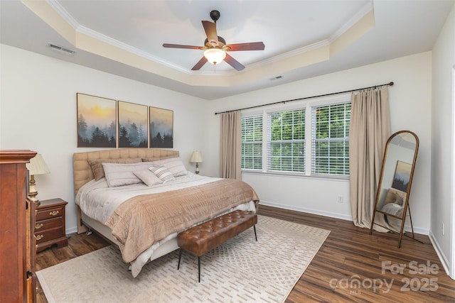 bedroom with a tray ceiling, baseboards, visible vents, wood finished floors, and crown molding