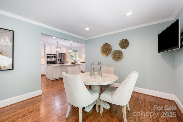 dining area with baseboards, crown molding, light wood-style flooring, and recessed lighting