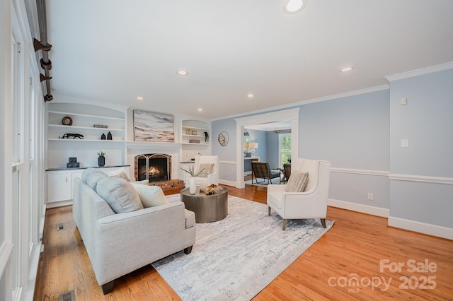 living area with light wood-style floors, baseboards, ornamental molding, a brick fireplace, and recessed lighting