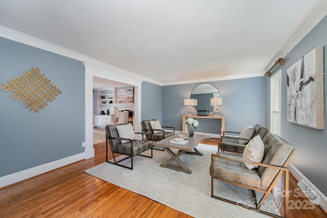 living room with light wood finished floors, baseboards, ornamental molding, and built in features