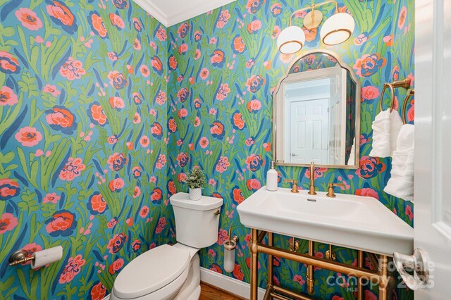 bathroom with wallpapered walls, toilet, baseboards, and crown molding
