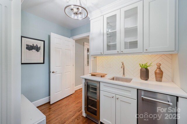 bar featuring a sink, decorative backsplash, beverage cooler, light wood-type flooring, and dishwasher