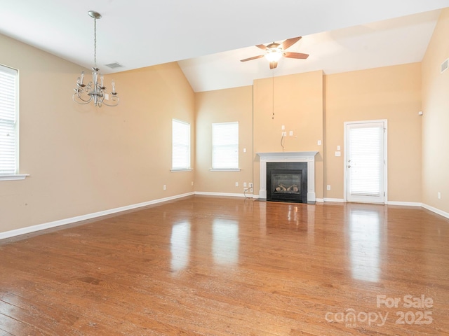 unfurnished living room featuring wood finished floors, vaulted ceiling, ceiling fan with notable chandelier, baseboards, and a fireplace with flush hearth