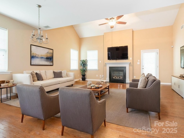 living room with a glass covered fireplace, light wood-style floors, visible vents, and ceiling fan with notable chandelier