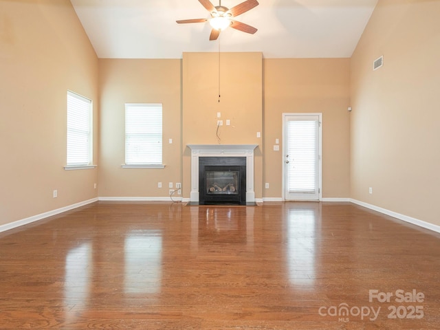 unfurnished living room with visible vents, wood finished floors, ceiling fan, and a fireplace with flush hearth