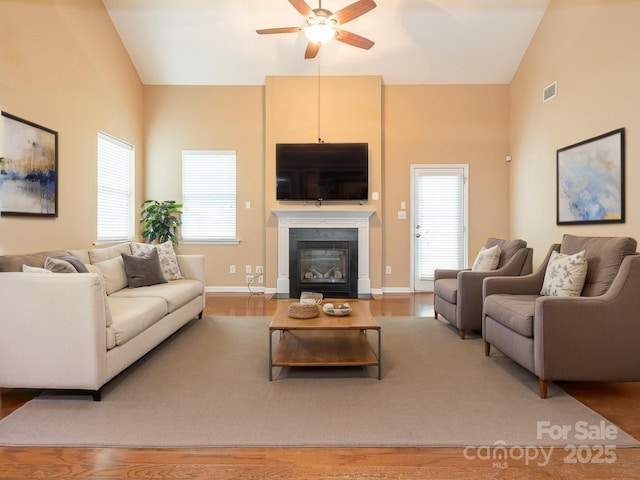 living room with a fireplace with flush hearth, visible vents, wood finished floors, a ceiling fan, and high vaulted ceiling