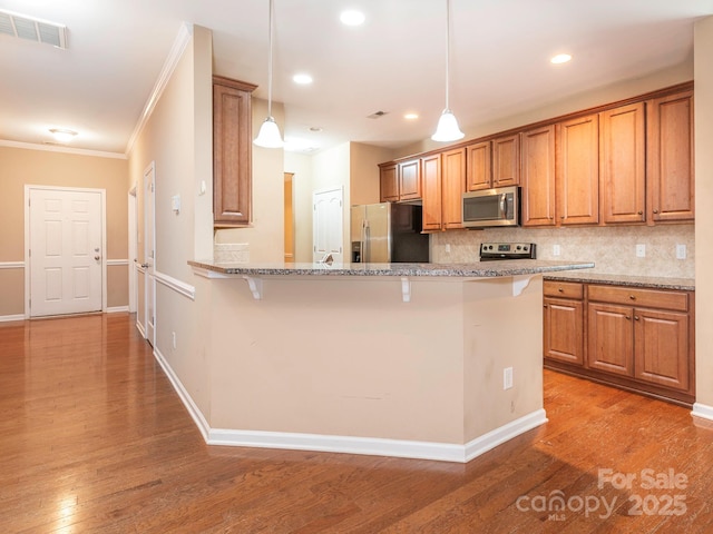 kitchen featuring decorative backsplash, stainless steel appliances, brown cabinets, a kitchen bar, and visible vents