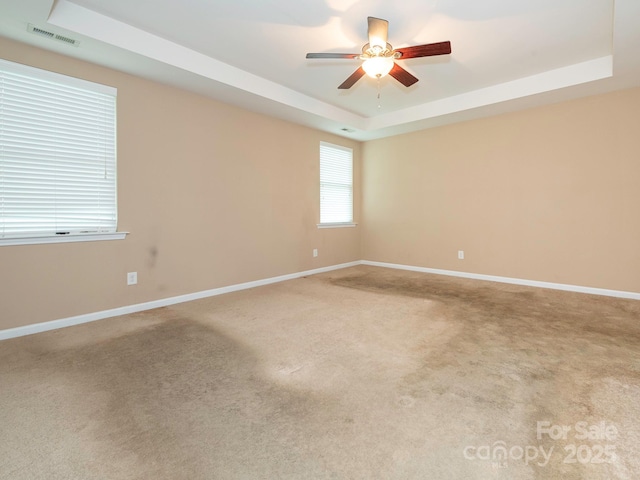 carpeted spare room with a raised ceiling, ceiling fan, visible vents, and baseboards
