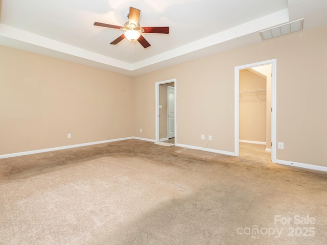 unfurnished room featuring a tray ceiling, a ceiling fan, visible vents, baseboards, and light colored carpet