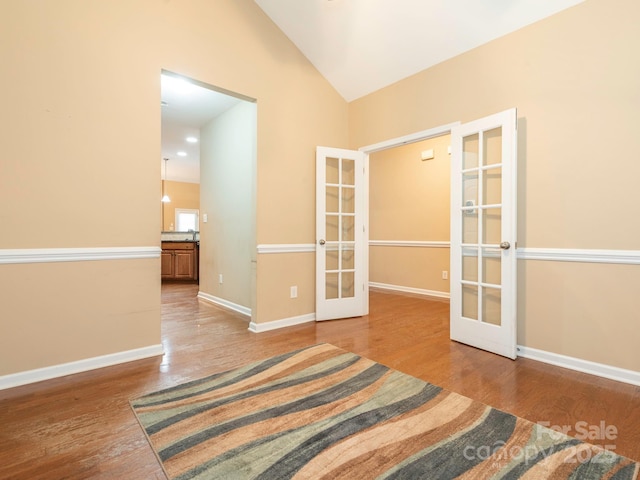 interior space featuring baseboards, wood finished floors, french doors, and vaulted ceiling