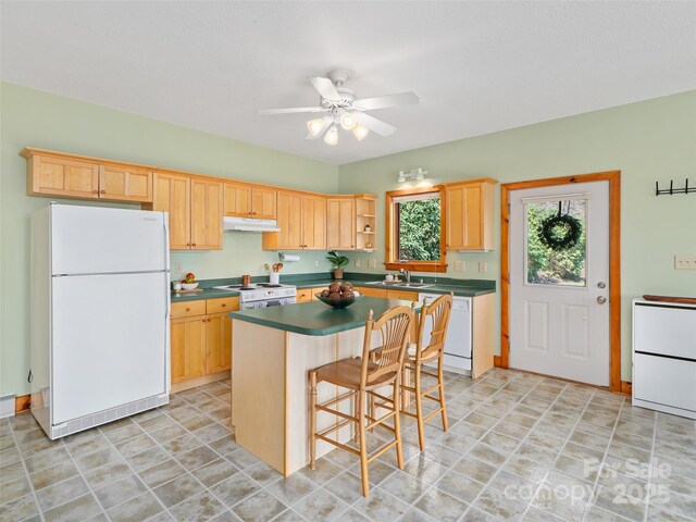 kitchen featuring dark countertops, a ceiling fan, white appliances, under cabinet range hood, and a kitchen island