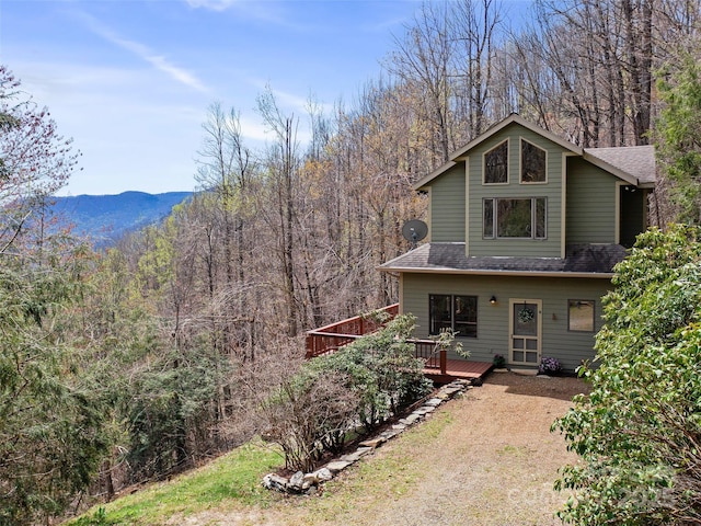 back of property featuring a wooden deck, roof with shingles, and a wooded view