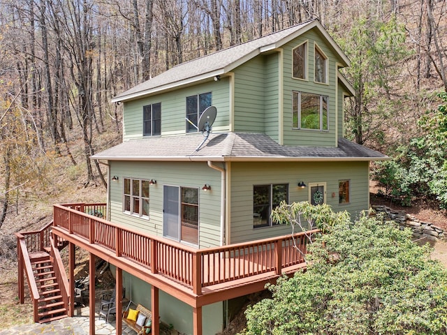 rear view of house with stairway, a patio area, a view of trees, roof with shingles, and a deck