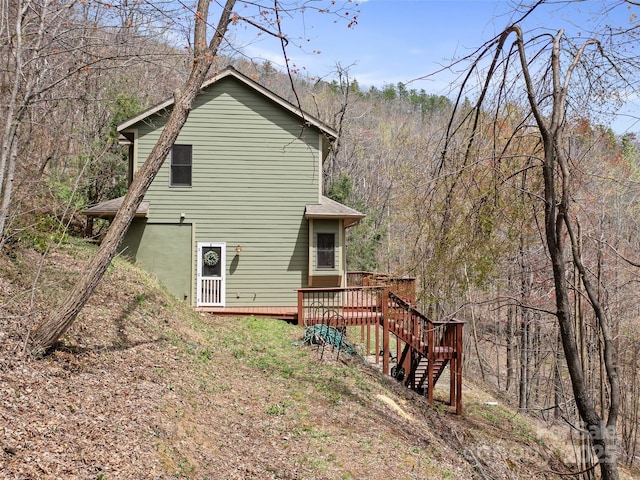 rear view of house with a forest view, stairway, a deck, and roof with shingles