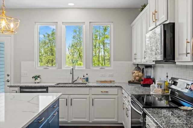 kitchen with white cabinets, stainless steel appliances, a sink, light stone countertops, and decorative backsplash