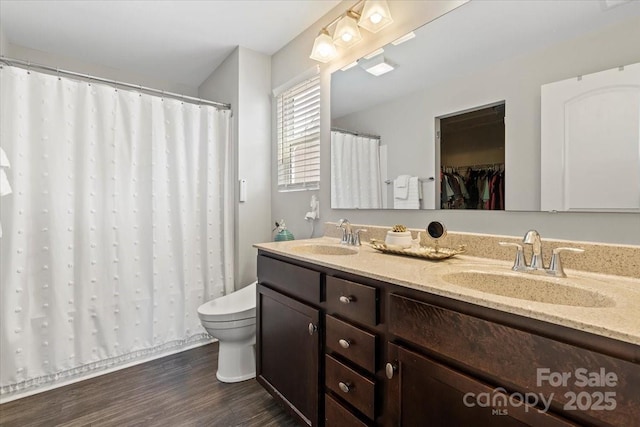 bathroom featuring double vanity, wood finished floors, toilet, and a sink