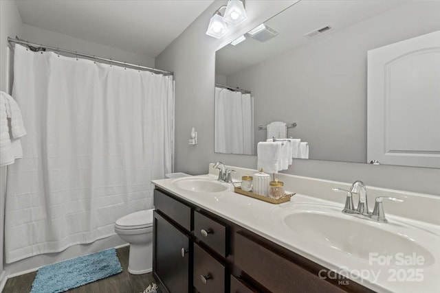 bathroom with toilet, wood finished floors, a sink, and visible vents