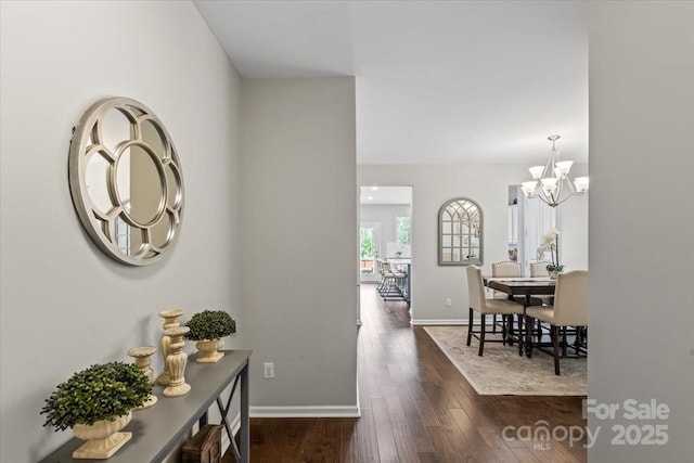 hallway featuring baseboards, dark wood-style floors, and an inviting chandelier