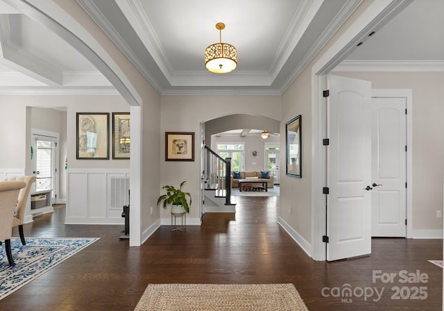 entryway with arched walkways, stairs, wood finished floors, and crown molding