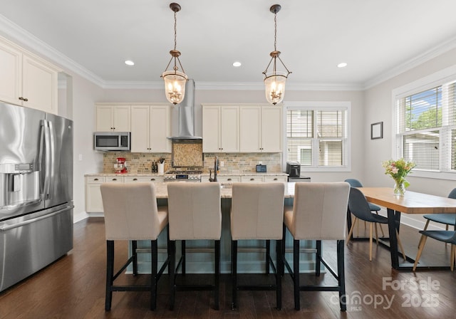 kitchen featuring wall chimney range hood, tasteful backsplash, stainless steel appliances, dark wood finished floors, and a center island with sink