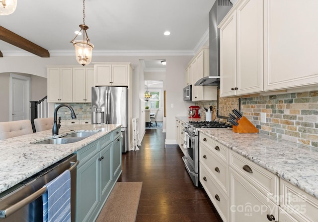 kitchen with wall chimney range hood, a sink, appliances with stainless steel finishes, recessed lighting, and hanging light fixtures