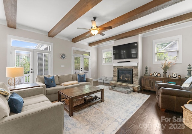 living room featuring dark wood-style floors, beam ceiling, french doors, a ceiling fan, and a stone fireplace