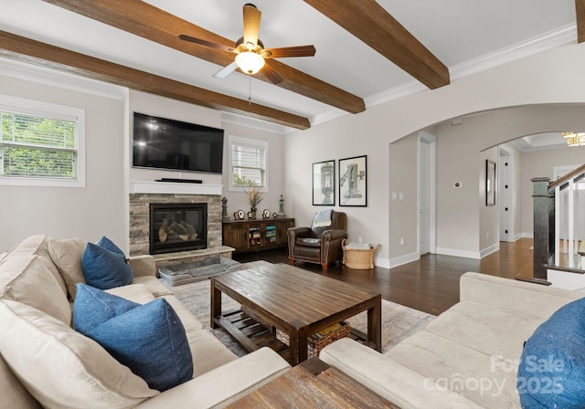 living area with arched walkways, wood finished floors, beamed ceiling, a stone fireplace, and a ceiling fan