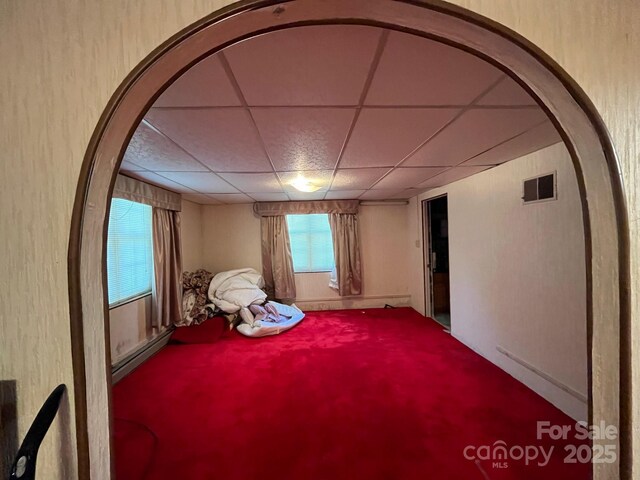 empty room with carpet floors, visible vents, arched walkways, and a paneled ceiling