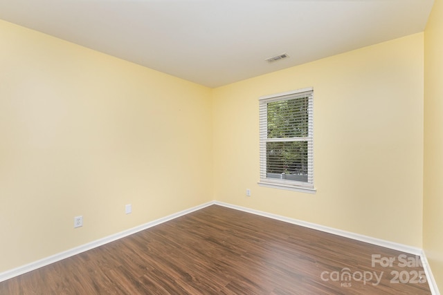 spare room featuring visible vents, dark wood-style flooring, and baseboards
