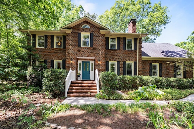 colonial-style house featuring a chimney and brick siding