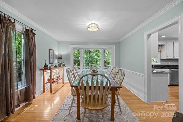 dining area with crown molding, light wood-style floors, and a wainscoted wall