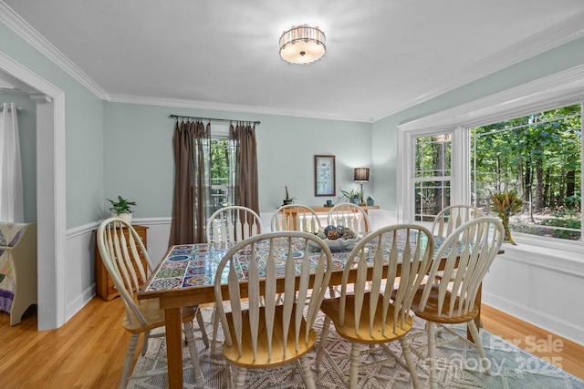 dining space with wood finished floors, crown molding, and wainscoting