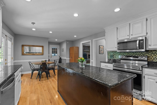 kitchen with appliances with stainless steel finishes, a kitchen island, white cabinetry, backsplash, and light wood-type flooring