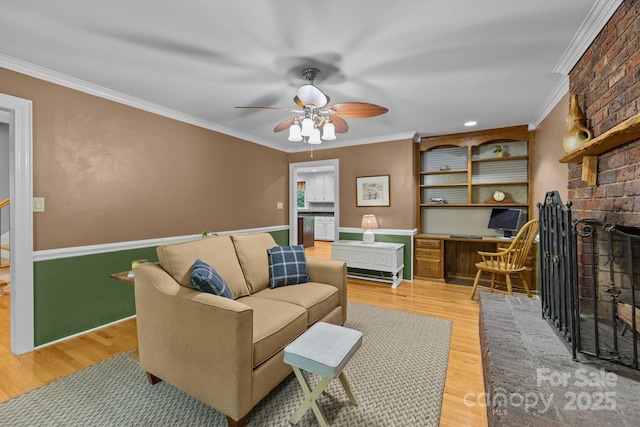 living room featuring crown molding, ceiling fan, light wood-type flooring, and a brick fireplace