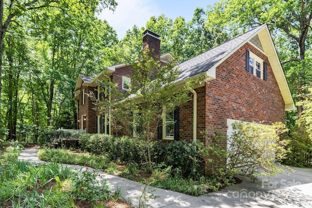 view of front of property with brick siding, a chimney, a garage, and a shingled roof
