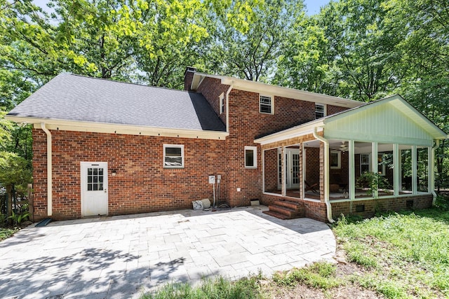 back of house with a patio, brick siding, roof with shingles, a sunroom, and a chimney