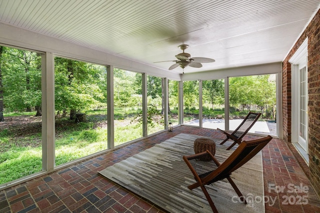 sunroom / solarium featuring a ceiling fan and brick flooring
