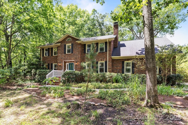 colonial inspired home featuring a chimney and brick siding