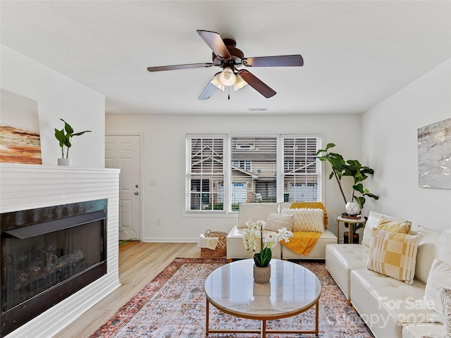 living area with visible vents, baseboards, light wood-type flooring, a fireplace, and a ceiling fan