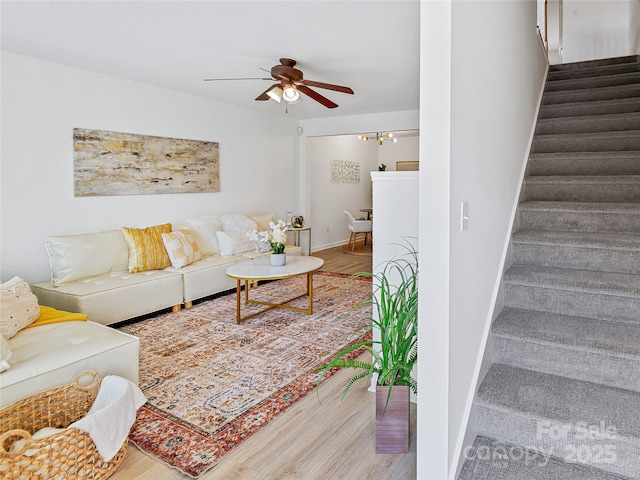 living area with stairway, wood finished floors, ceiling fan, and baseboards
