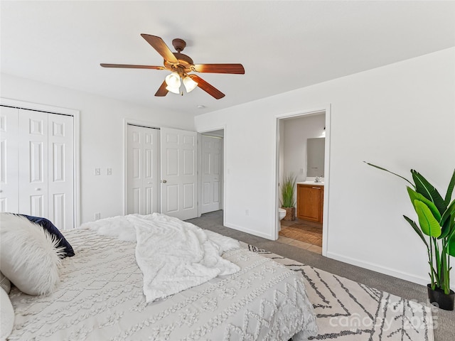carpeted bedroom featuring baseboards, ensuite bathroom, a ceiling fan, and two closets